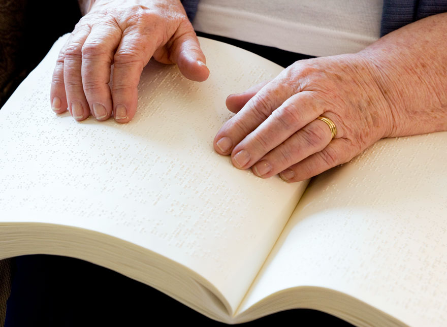 An elderly person's hands reading a Braille book.