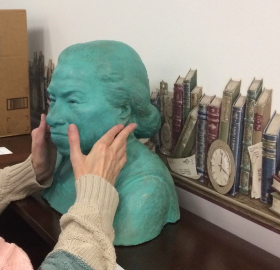 Person's hands on a sculpture of a human face