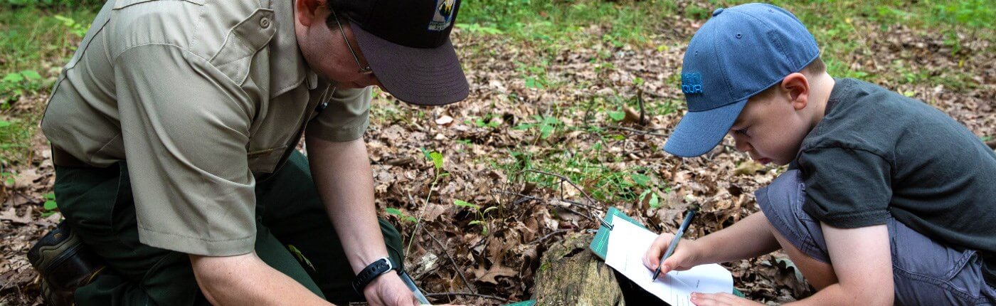 Adult and child in wooded area writing on paper